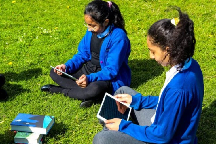Pupils using tablets while sitting on grass