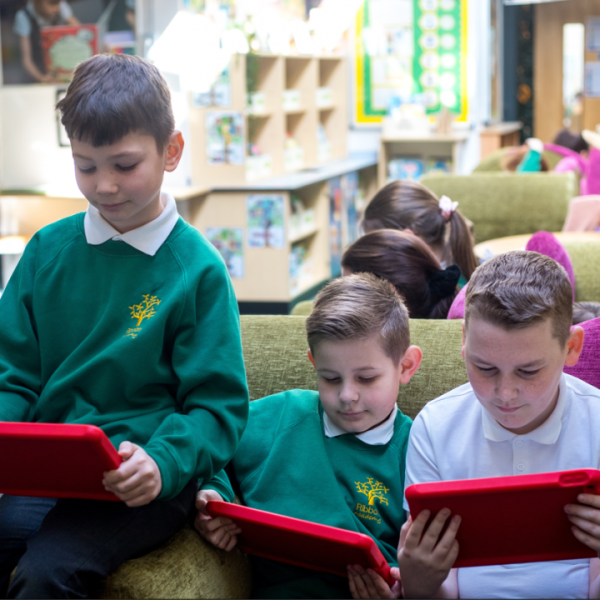 Three children using tablets on a sofa